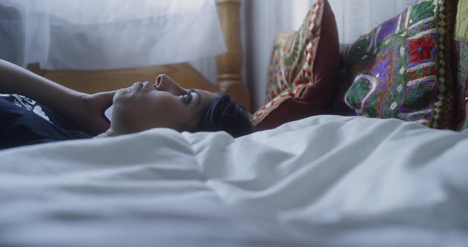 A woman drops down onto her bed while talking on the phone