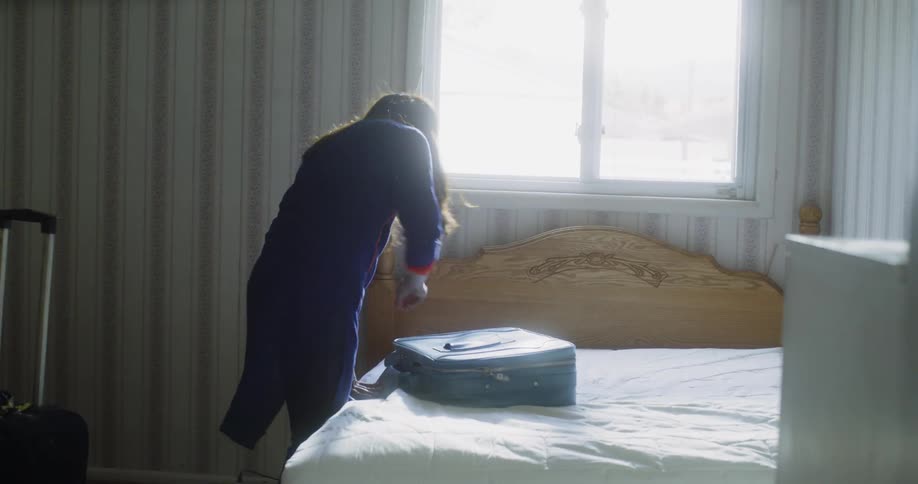 A woman unzips a suitcase on a bed