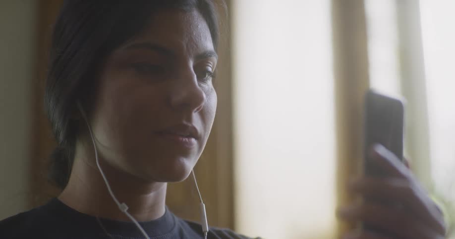 Woman with earphones looking at her phone and reacting in a surprised way