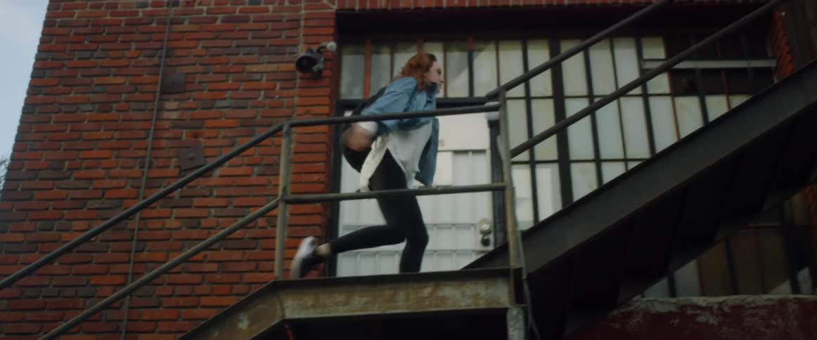 A woman walks up a metal staircase to a brick building