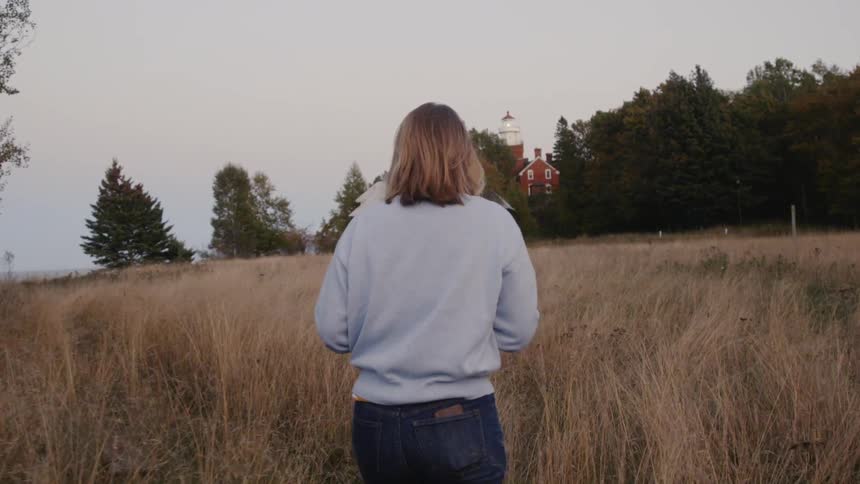 A woman walks through a field while watching the sunset behind the trees
