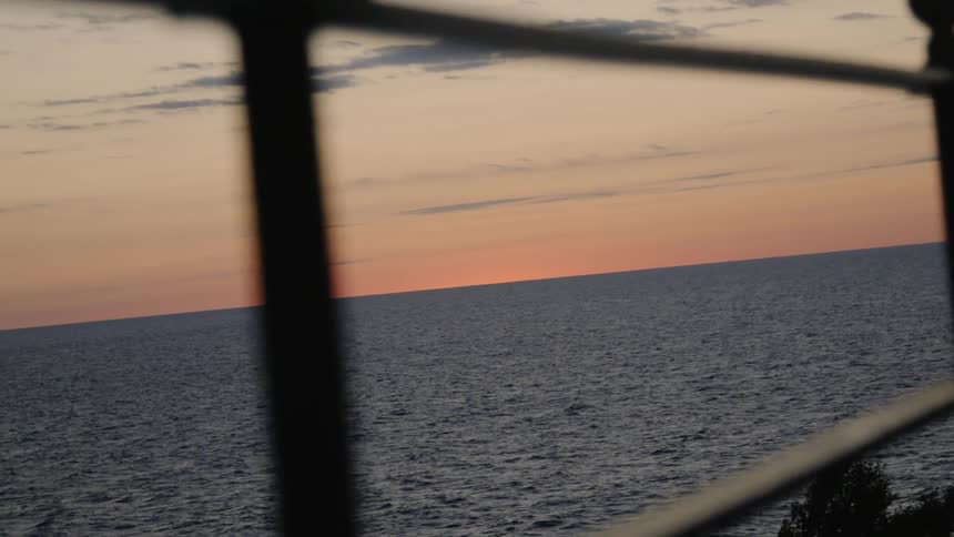 The sun sets behind an ocean as the sky turns pink