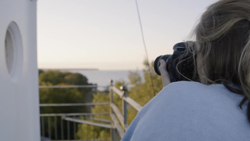 A female photographer using her camera pointed at a body of water