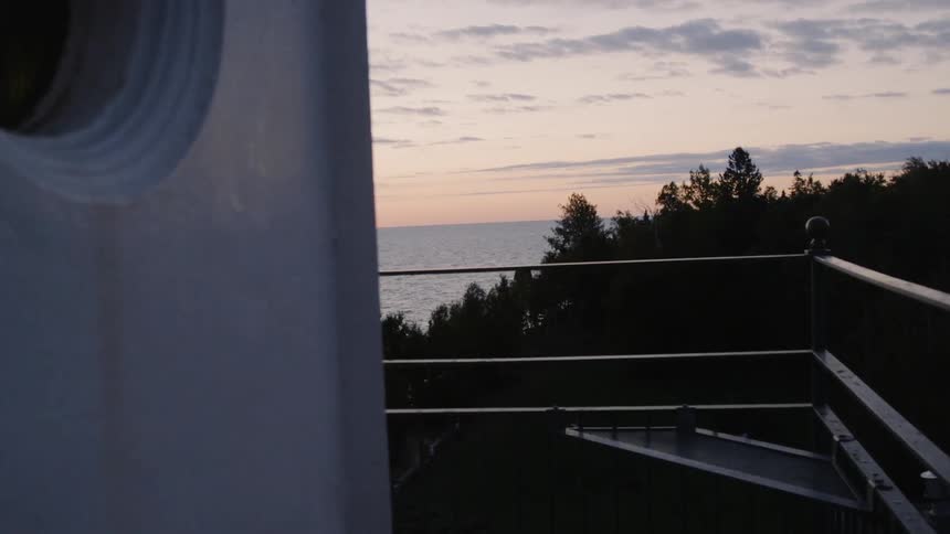 The ocean flows and trees stand below a high porch