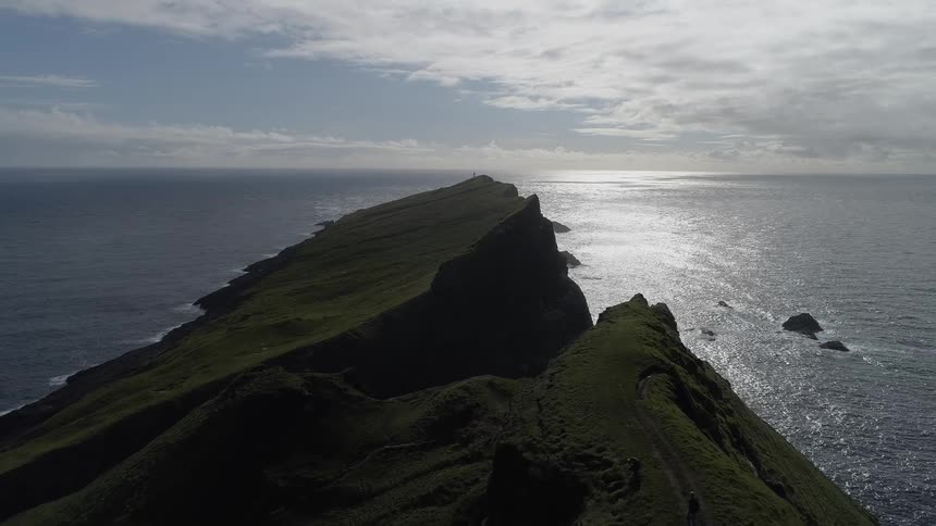 A large grass covered rocky cliff stands in the ocean