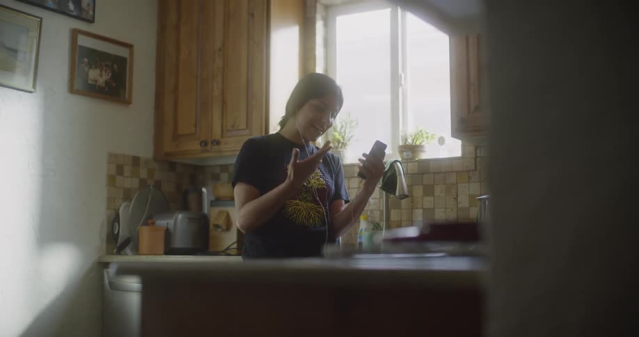 A woman has a conversation on video chat while standing in the sunlight from a nearby window