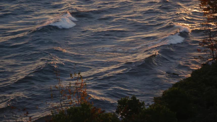 Rolling waves crash into the bushes and rocks of a shoreline at fall