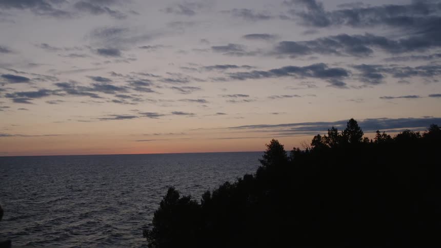 The ocean flows toward a forest at sunset