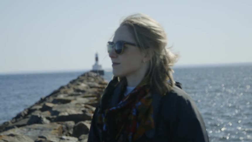Woman stands on a rocky beach with a beacon in the back