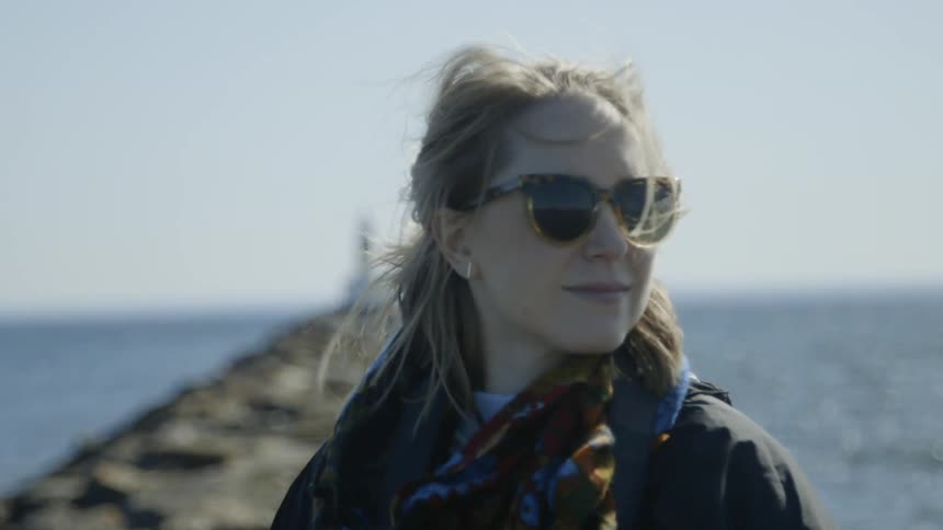 Woman smiling and standing next to a pier with a lighthouse close