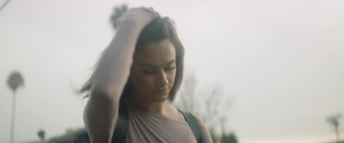 A woman with a backpack on runs her hand through her hair as she walks under power lines