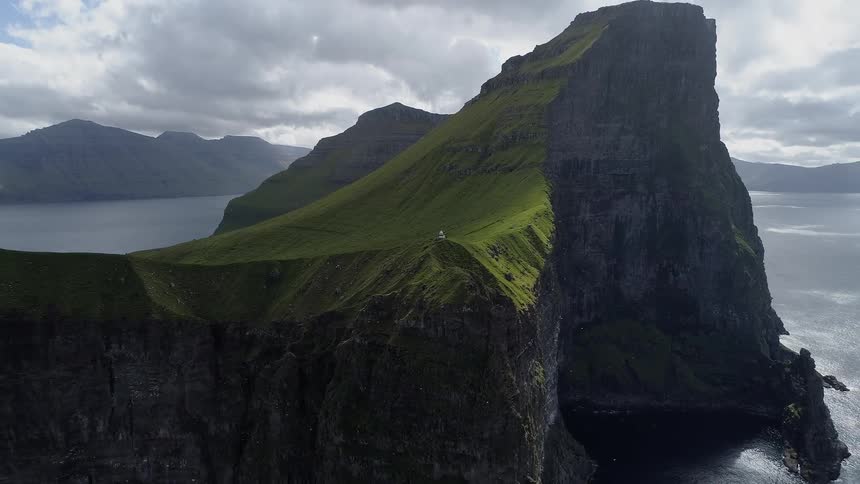 A small house on a grassy hill next to a big rocky cliff