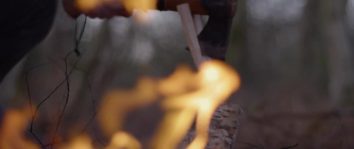 Someone cutting small pieces of wood next to a campfire