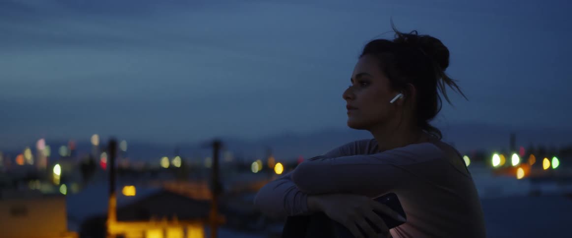 A woman sitting outside with earbuds in her ears