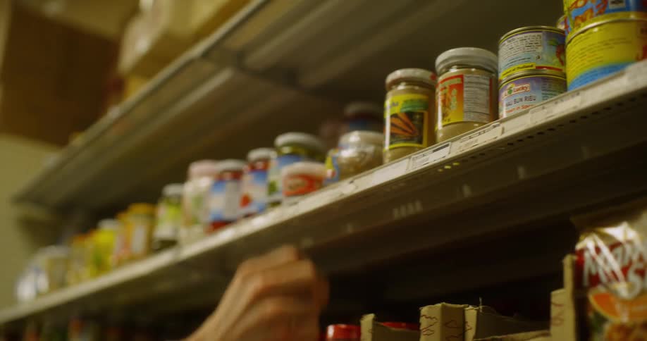 A person looks at different spices on supermarket shelves before picking one up and putting it back on the shelf
