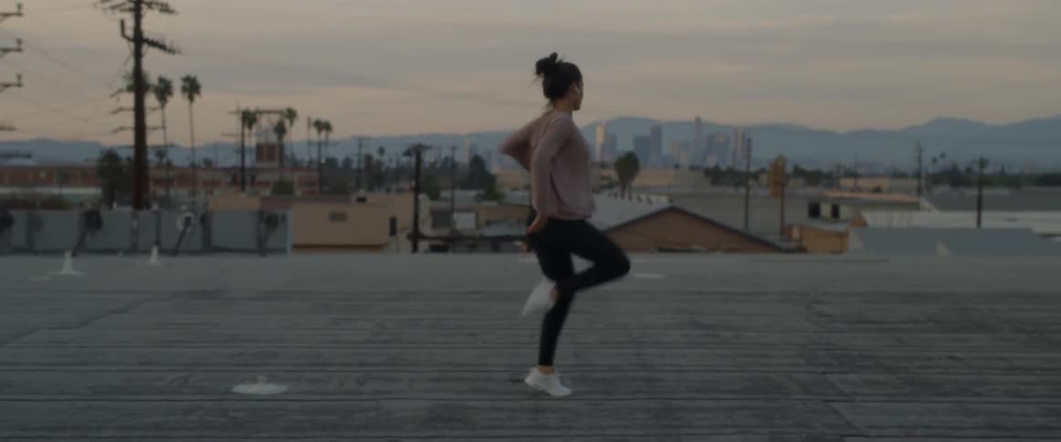 A woman wearing ear buds dances on a rooftop