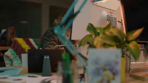 Woman gets up from her desk and walks away while another woman sits at her desk laughing