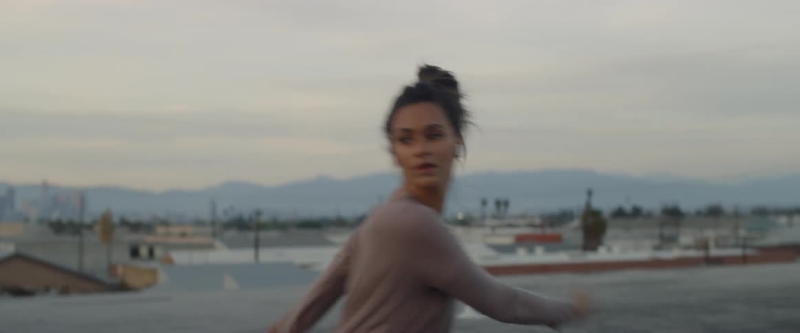 Woman wearing earphones dancing on a city rooftop