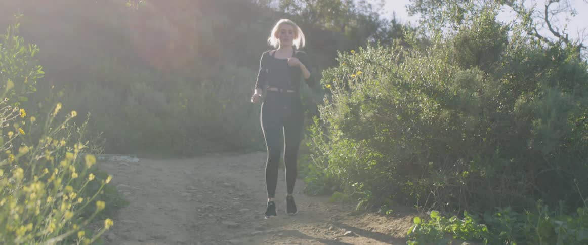 A woman jobs down a dirt path with foliage to both sides of her