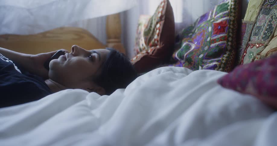 A woman laying on her bed talking on the phone suddenly sits up