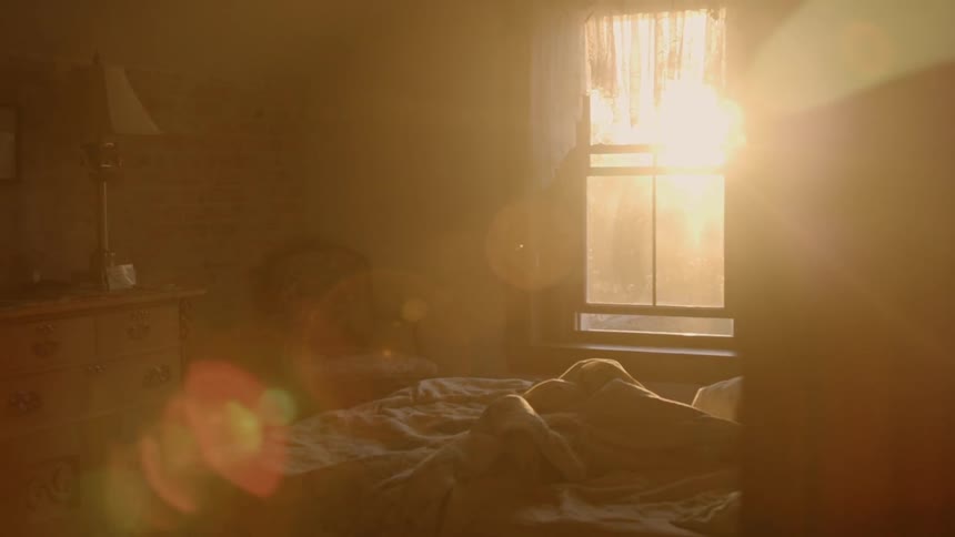 The sunrise shines through the window onto an unmade bed
