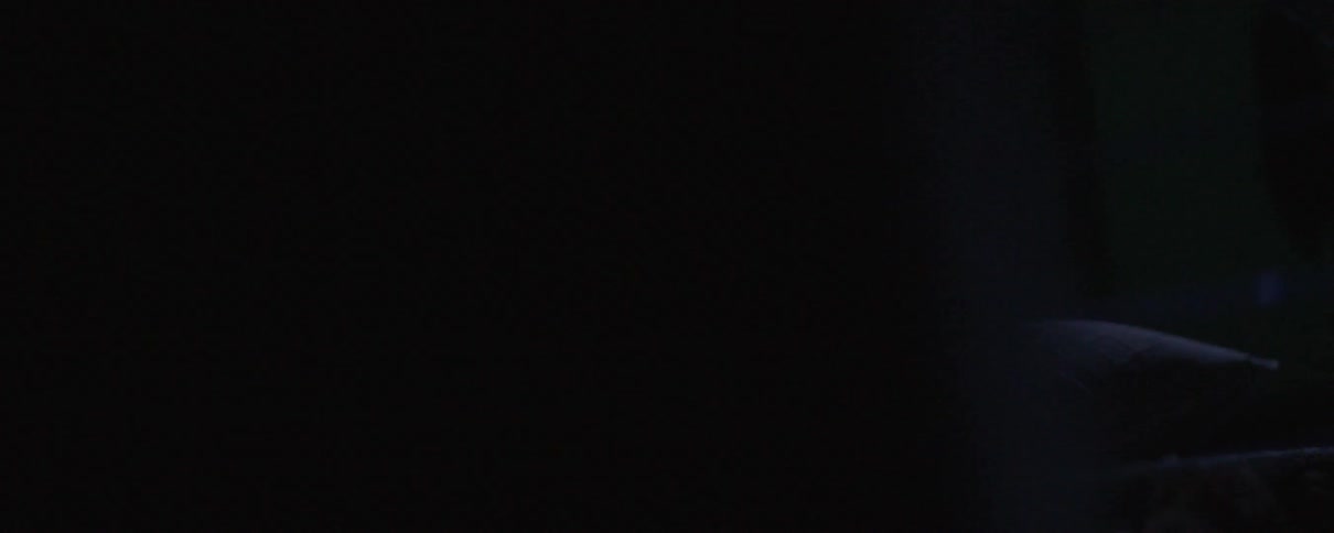 A man lays in darkness with his shirt off while his chest and face are slightly lit up