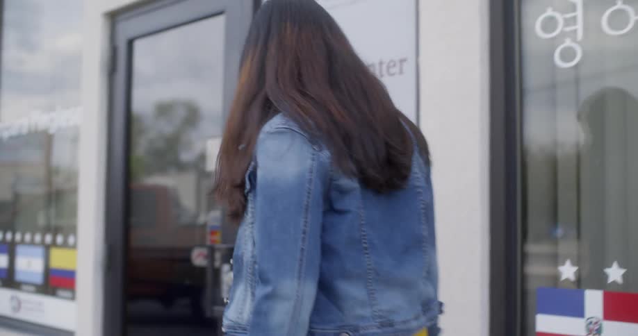 A woman walking next to a building and opening the door to head in