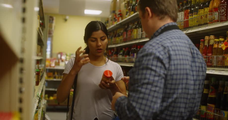 A woman points at and talks about a product in a supermarket to a man