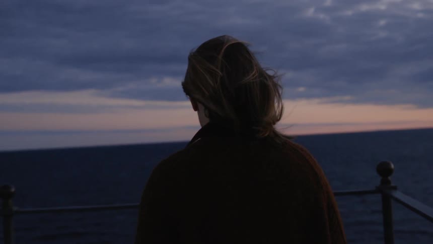 Woman walking with her hair in the wind while looking at a sun setting at sea