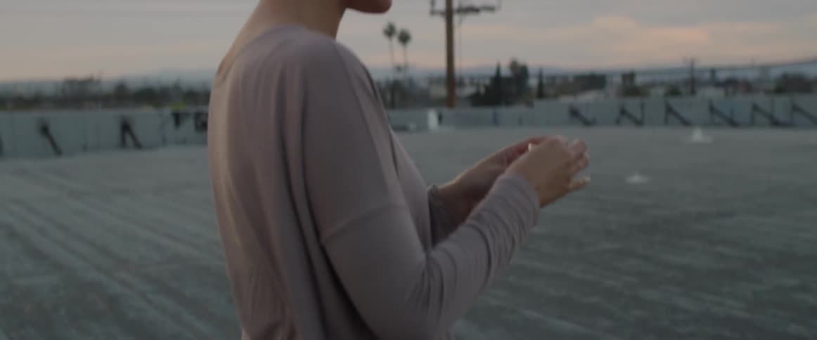 A woman on a rooftop takes her phone out of her purse then puts earbuds in her ears