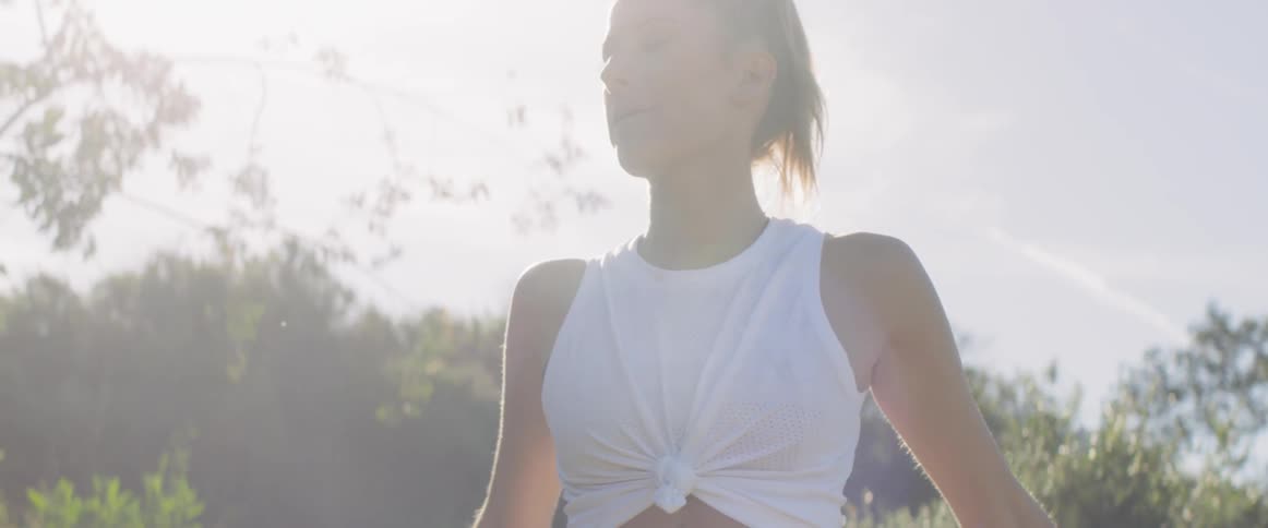 A woman crosses her arms and stretches under a brilliant sun