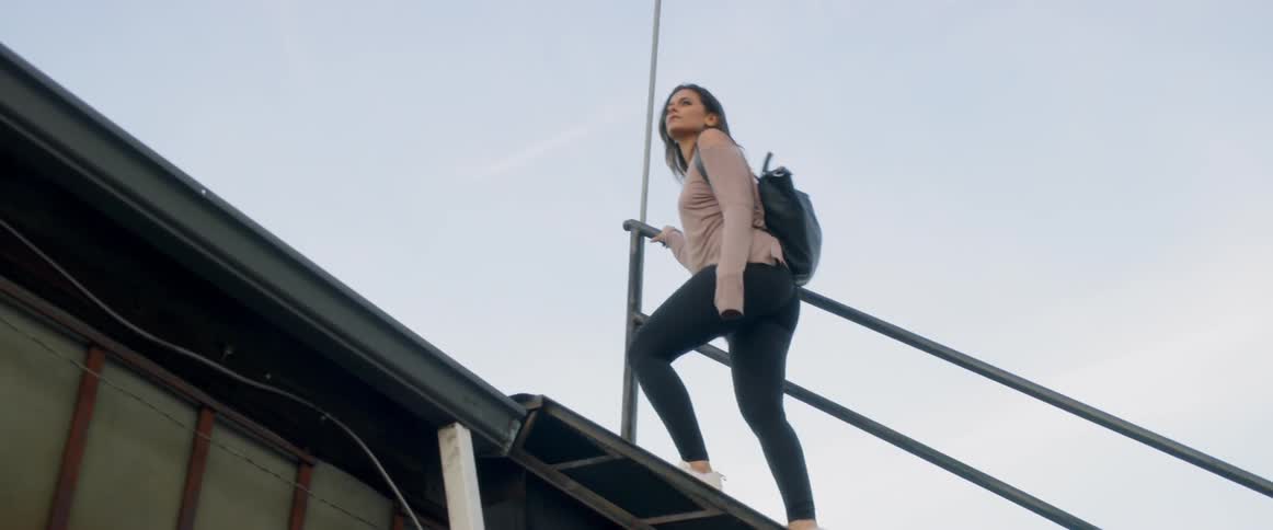 A woman wearing a backpack climbs up stairs on to a roof