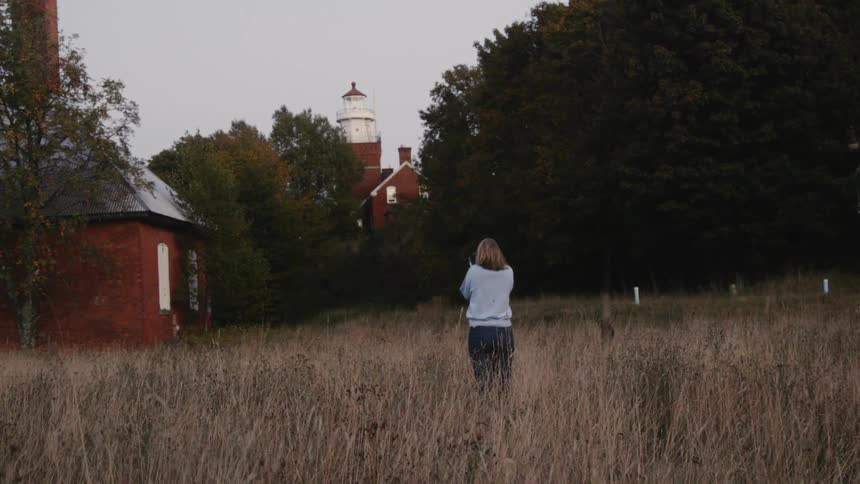 A woman stands in a field staring off into the sunset