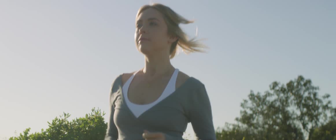 A woman jogs in the sunlight with a clear sky above her