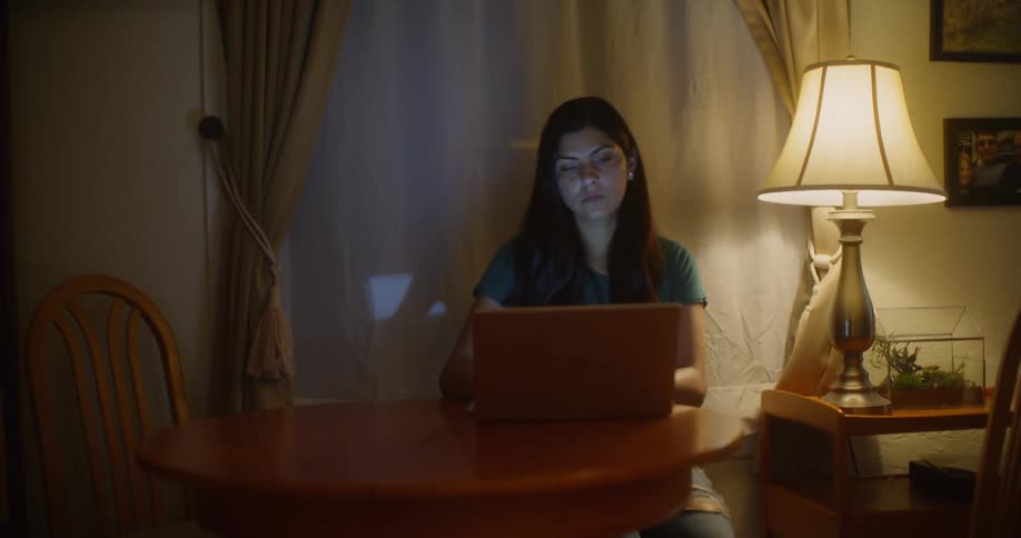 Woman sits at a small table looking at a laptop