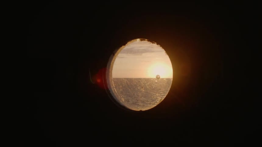 Looking at the sun over the sea through the peephole of a ship