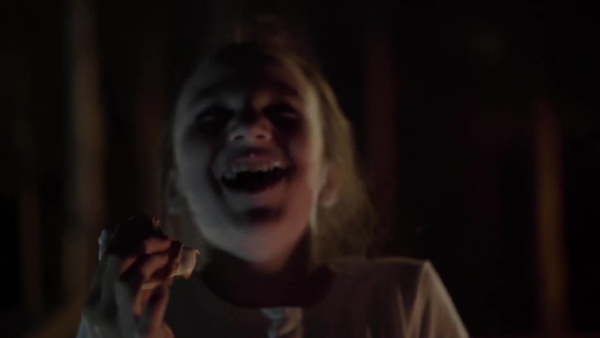 A little girl takes a bite of a smore by the fireside as she laughs