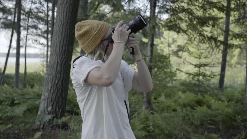 A woman taking a photo of a tree in a forest with a large camera