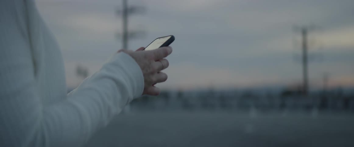 Woman with headphones types on her phone outside