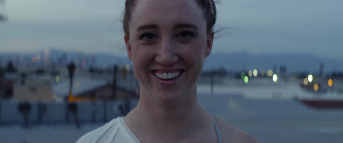 A woman stands smiling and then laughing as she stands on a rooftop