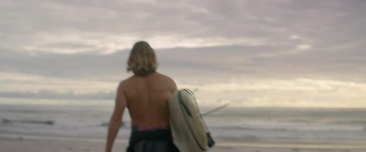 Man carrying a surfboard walks on the beach on a cloudy day