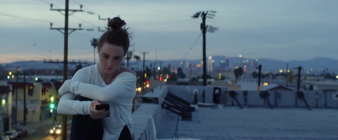 A woman sitting on the edge of a rooftop looking at her phone