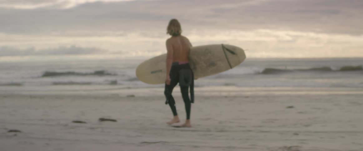 A surfer carries his surfboard on the beach
