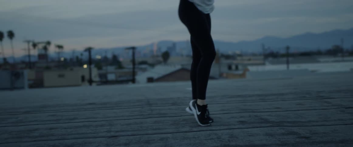 A woman dances outside at sunset with buildings and mountains in the background
