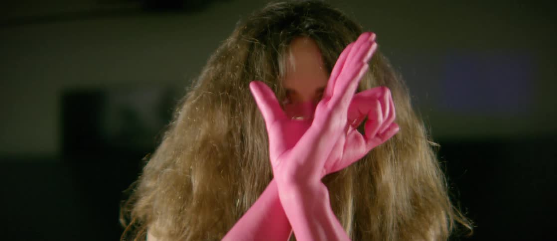 A woman with her forearms and hands painted pink does an interpretive dance in a spotlight