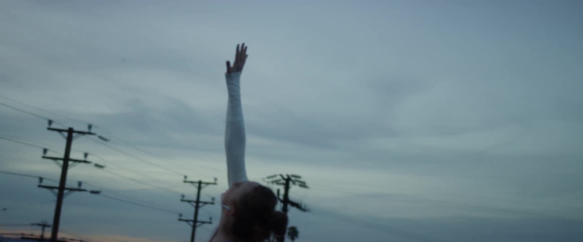Woman stretches her arm upwards as she stands outdoors