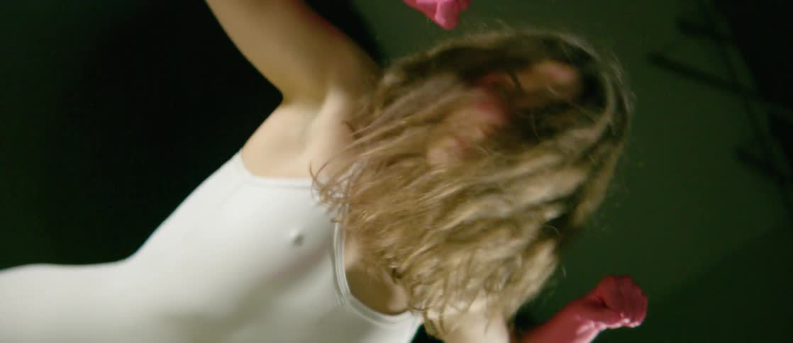 A woman with her forearms and hands painted pink does an interpretive dance in a spotlight