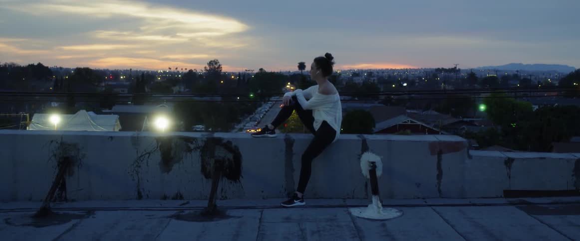 Woman sits on a rooftop ledge looking out at a town