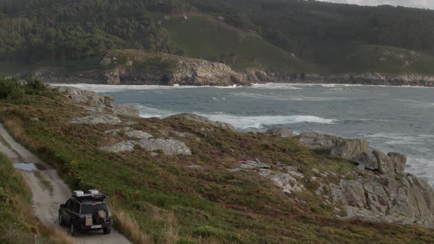 A truck driving on a dirt road next to a rocky beach