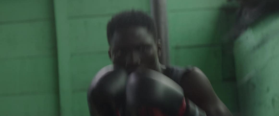 A young man quickly punches a speed bag in a room with concrete walls